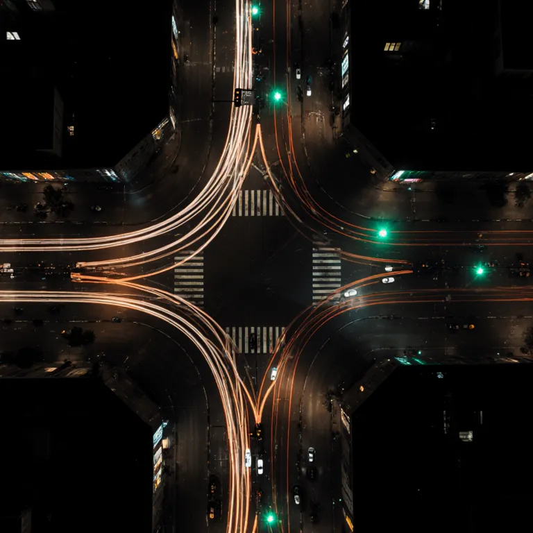 Aerial time-lapse of a city intersection at night, car light trails forming a routing web
